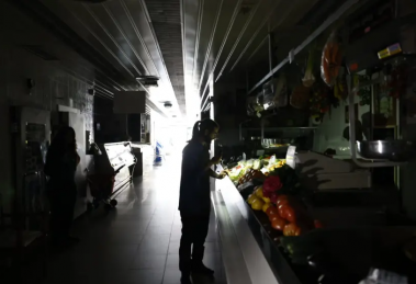 Una mujer mirando unas frutas y verduras con su linterna del móvil a oscuras
