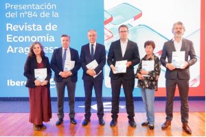 Seis personas posan en el escenario durante la presentación del número 84 de la Revista de Economía Aragonesa, organizada por Ibercaja. Cada una sostiene un ejemplar de la revista frente a un fondo azul con el nombre del evento.